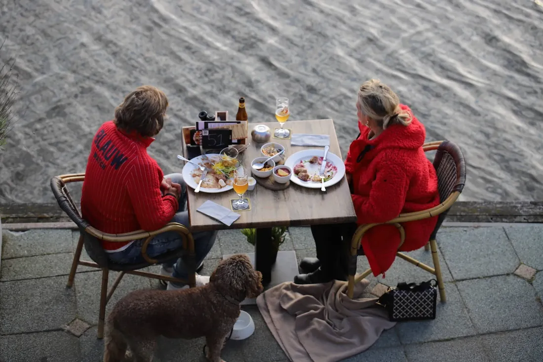 Choir on the pont: 2 guests at a table by the water, the dog under it