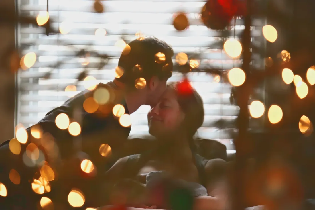 A kiss on the forehead through the Christmas lights
