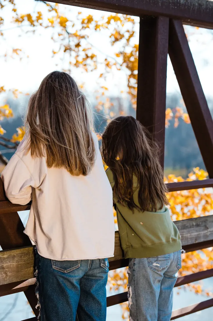 Two sisters at the rail, fall leaves ahead