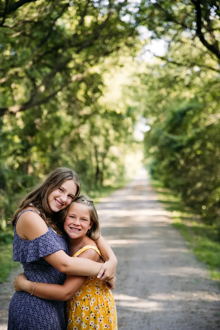 Sisters hugging on a leafy path