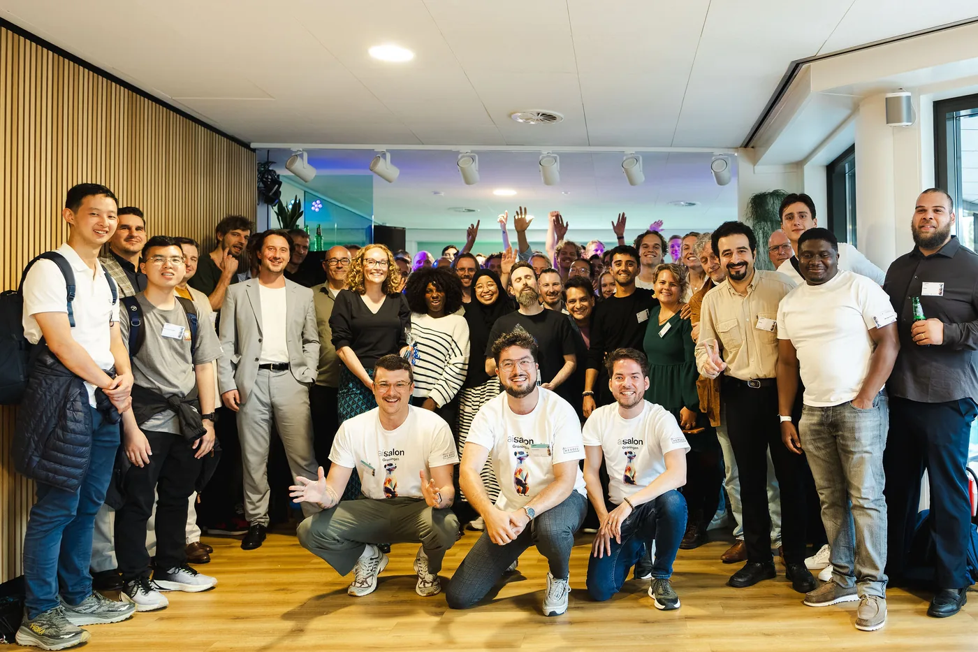 The AI Salon Groningen crowd in a group photo, hosts crouching at the front in AI Salon T-shirts
