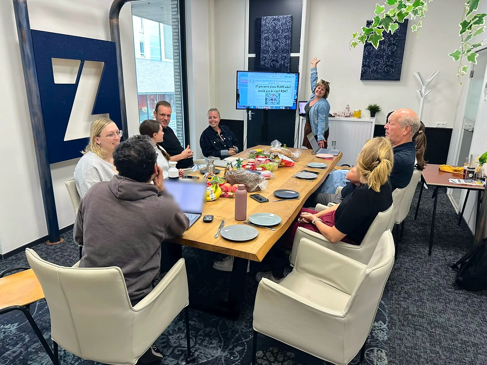 Members around a long lunch table while Alex points at a question on the screen