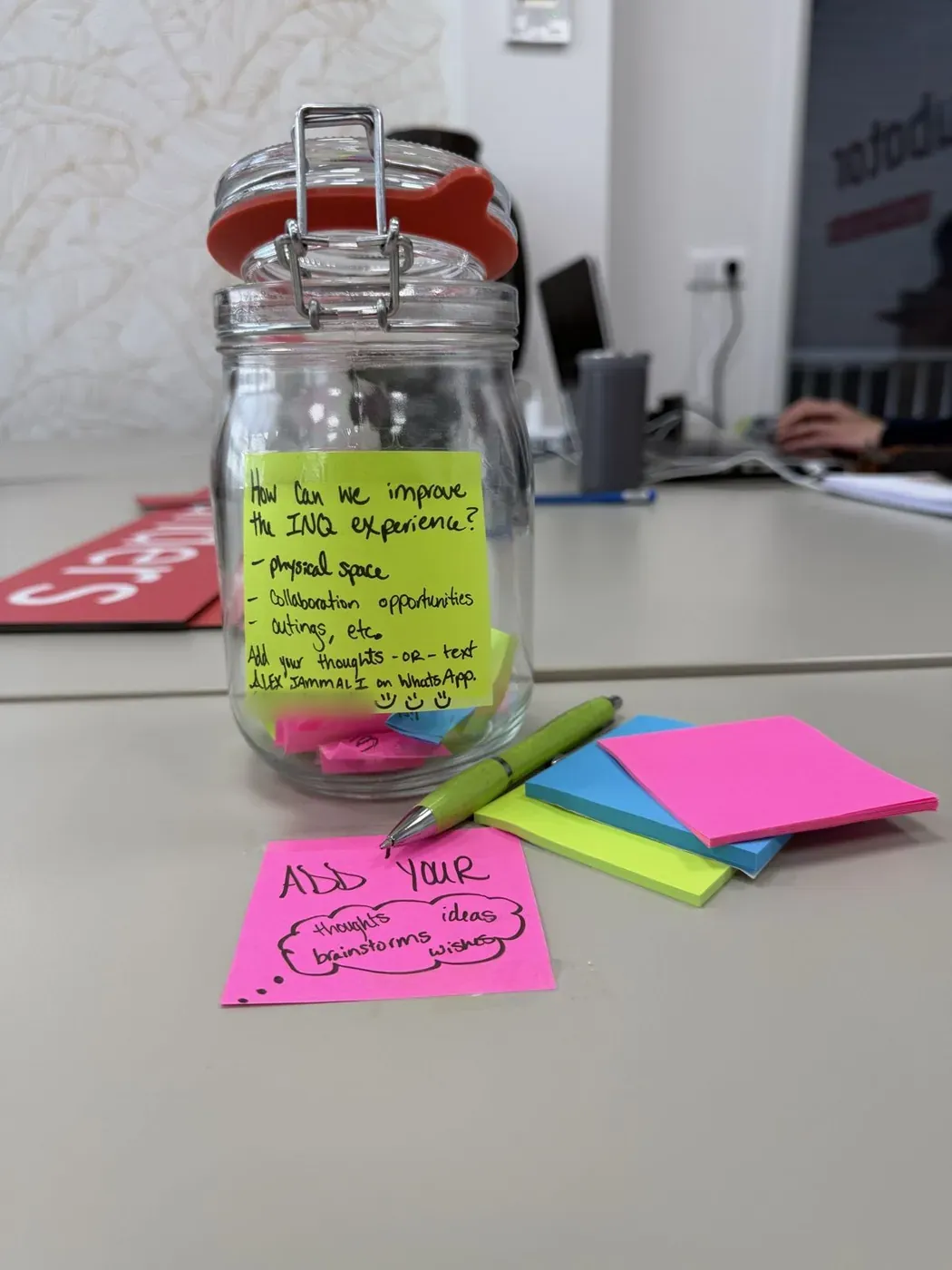 A glass jar of sticky notes on a desk, with a note asking how to improve the INQ experience