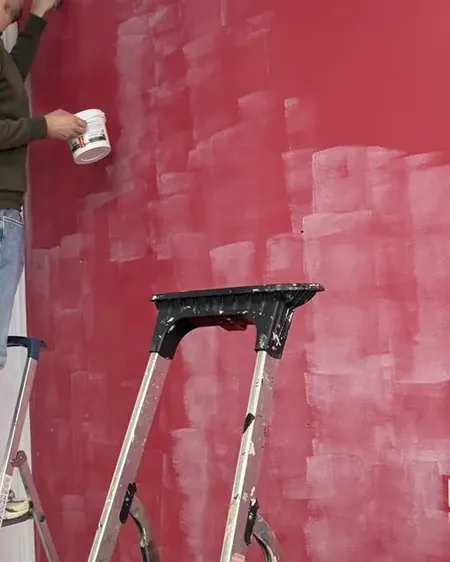 A wall halfway through its first coat of red paint, with a stepladder in front