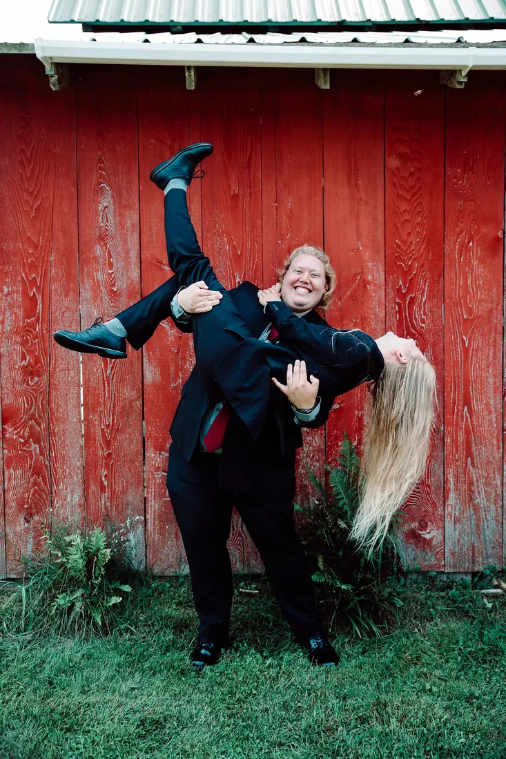Amanda & Jack: the groom, lifted upside down against the red barn