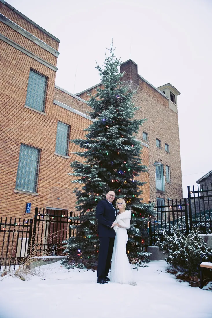 Patty & Craig: under a snowy fir by the old brick building