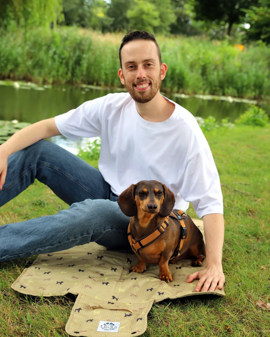Robert sitting on the grass by the water with his dachshund on a PawsOnTheGo mat